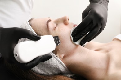 Photo of Cosmetologist using ultrasonic scrubber, closeup. Client having cleansing procedure indoors