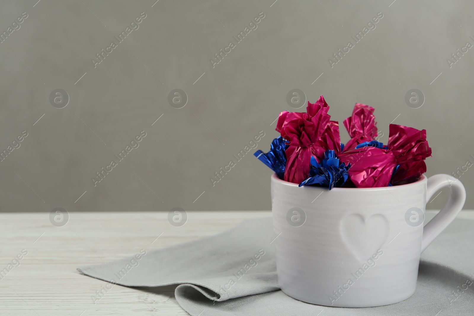 Photo of Candies in colorful wrappers on white wooden table. Space for text