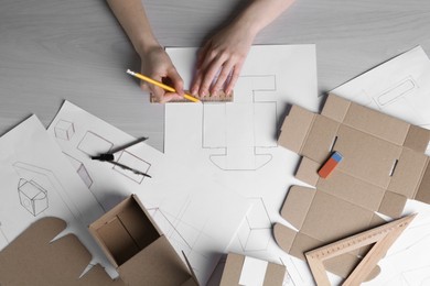 Woman creating packaging design at light wooden table, top view