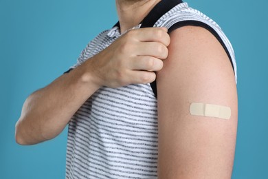 Photo of Vaccinated man showing medical plaster on his arm against light blue background, closeup