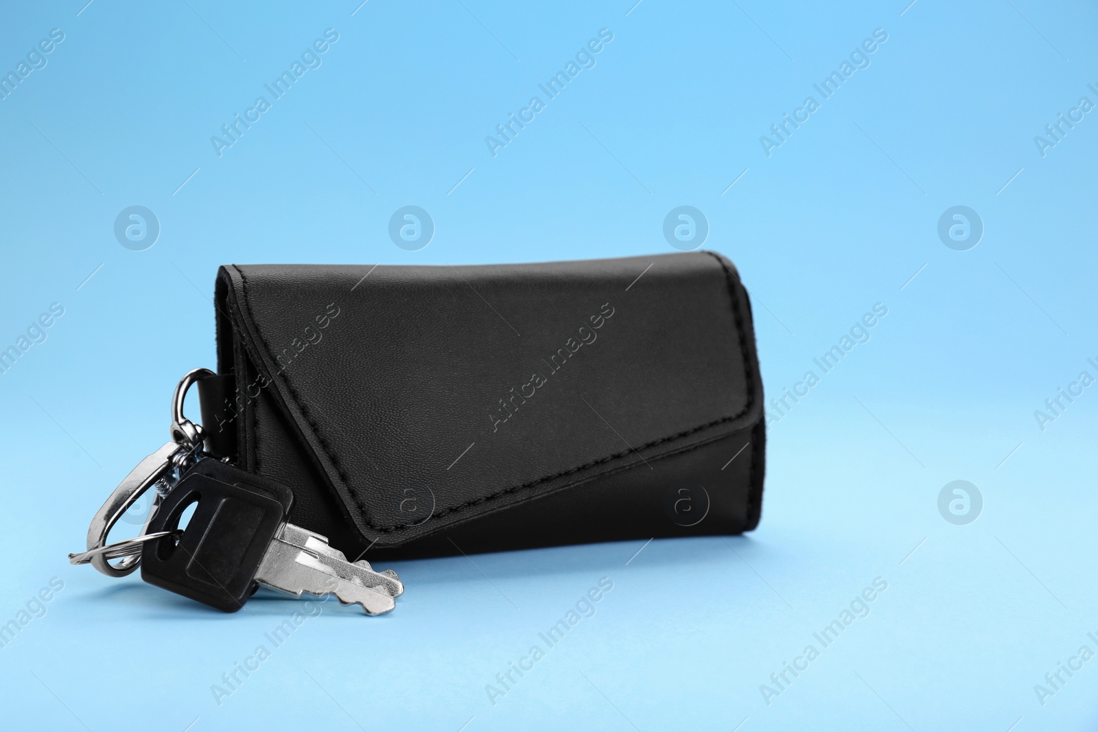 Photo of Leather case with keys on light blue background. Space for text