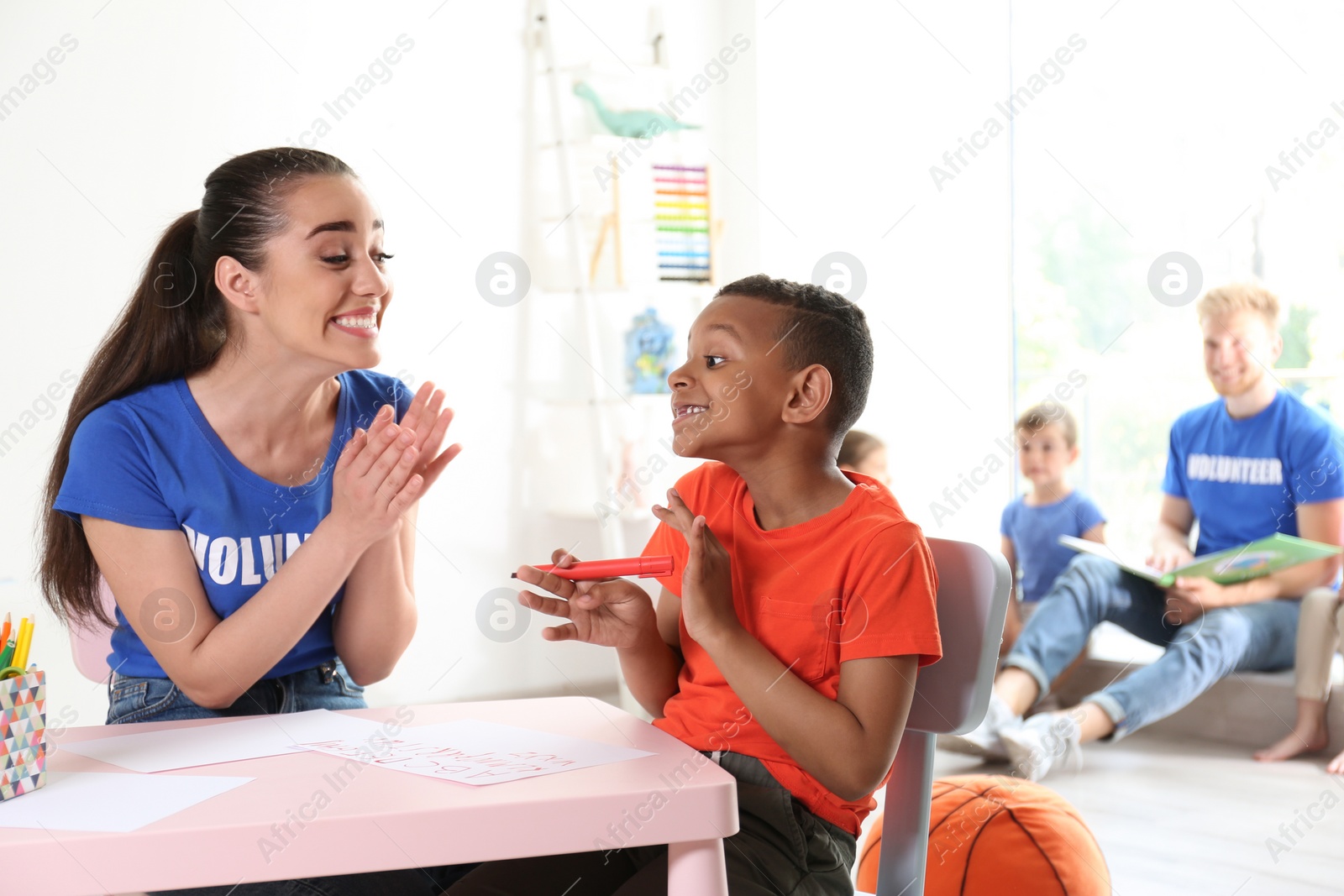 Photo of Little African-American boy learning alphabet with volunteer at table indoors