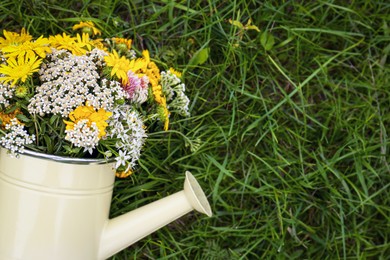 Photo of Pale yellow watering can with beautiful flowers on green grass, top view. Space for text