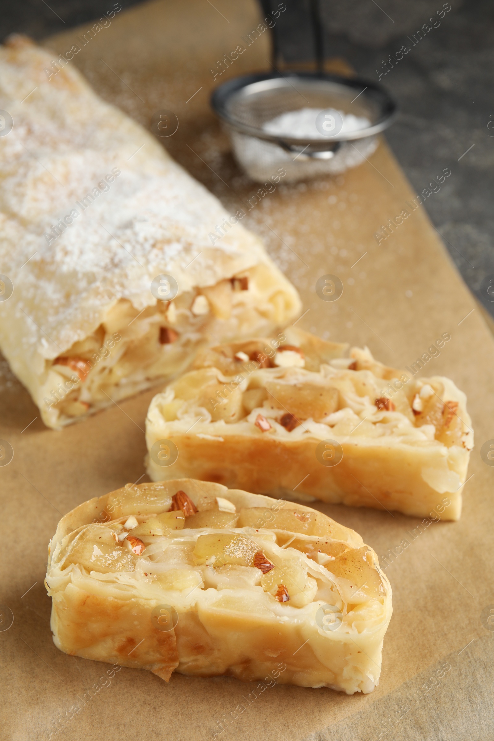 Photo of Delicious apple strudel with almonds on parchment, closeup