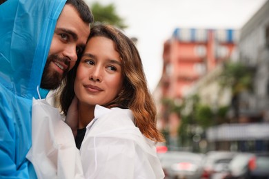 Photo of Young couple in raincoats enjoying time together on city street, space for text