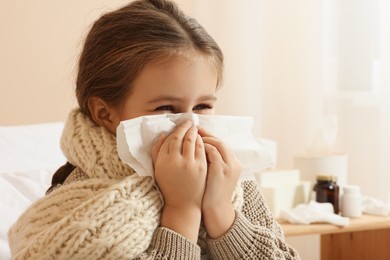 Photo of Girl blowing nose in tissue on bed in room. Cold symptoms