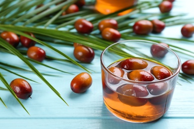 Palm oil in glass, tropical leaves and fruits on light blue wooden table