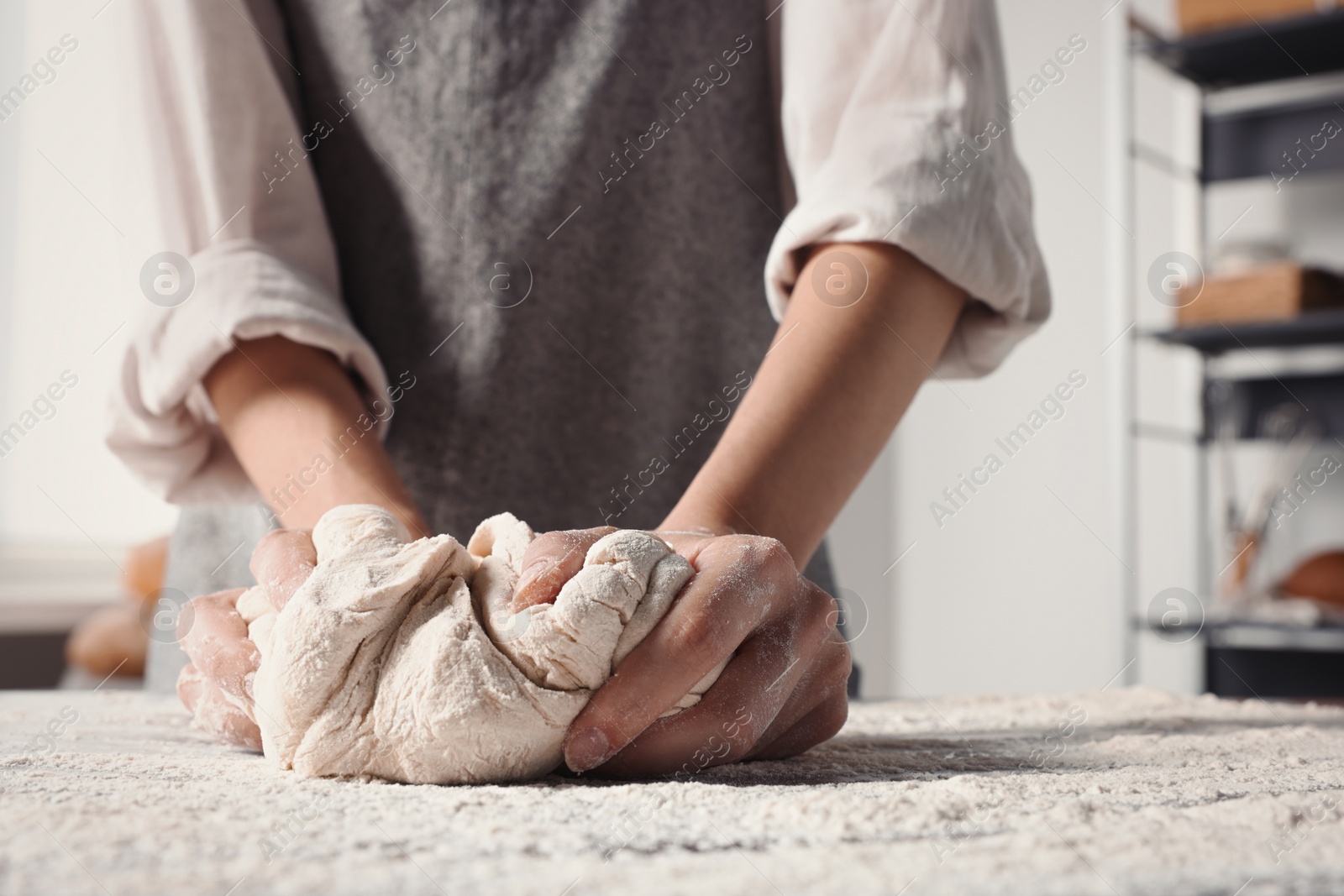 Photo of Woman kneading dough at table in kitchen, closeup