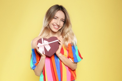 Portrait of beautiful smiling girl with heart shaped gift box on yellow background. International Women's Day