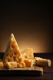 Photo of Pieces of delicious cheese and knife on wooden table. Space for text