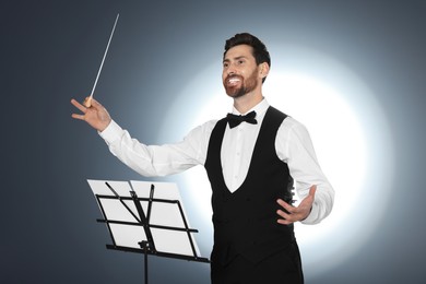 Happy professional conductor with baton and note stand on grey background