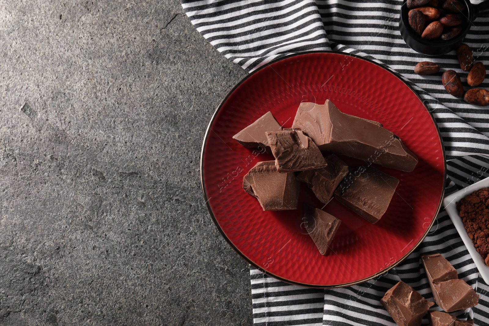 Photo of Pieces of tasty milk chocolate and cocoa beans on grey table, top view. Space for text