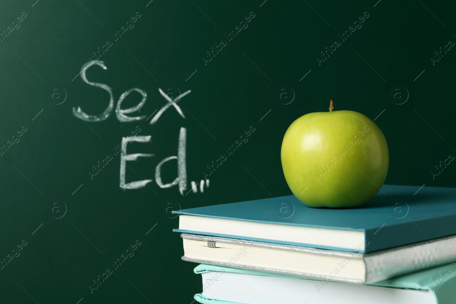 Photo of Books and apple near chalkboard with phrase "Sex ed"