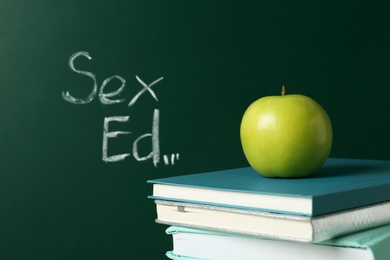 Books and apple near chalkboard with phrase "Sex ed"