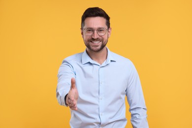 Photo of Happy man welcoming and offering handshake on yellow background