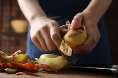 Photo of Woman peeling fresh potato at table indoors, closeup