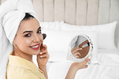 Beautiful woman with mirror applying makeup in bedroom