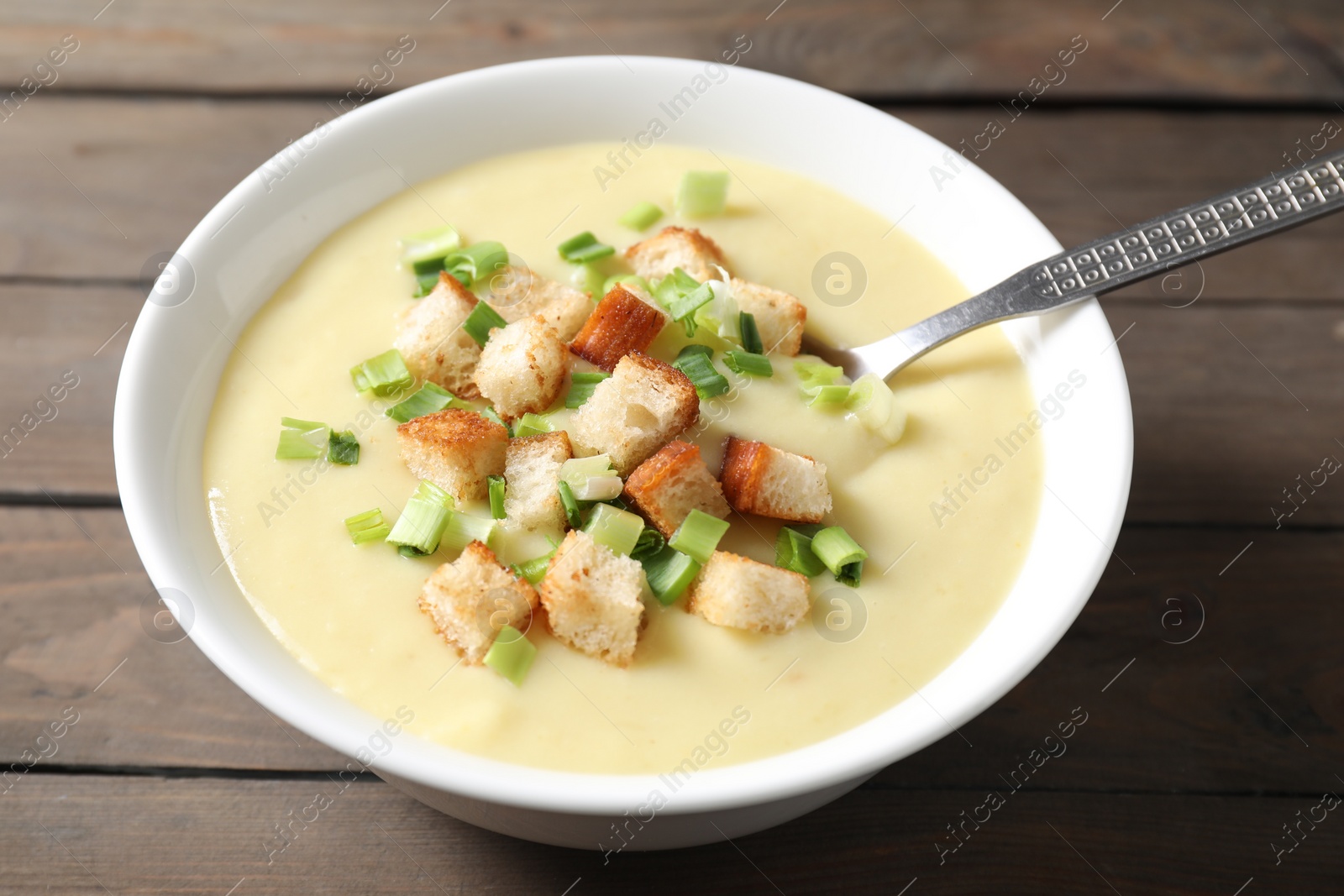 Photo of Tasty potato soup with croutons and spoon in bowl on wooden table