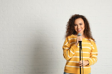 Photo of Portrait of curly African-American woman in sweater posing with microphone near brick wall. Space for text