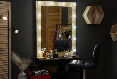 Makeup room. Stylish mirror near dressing table with beauty products and chair indoors