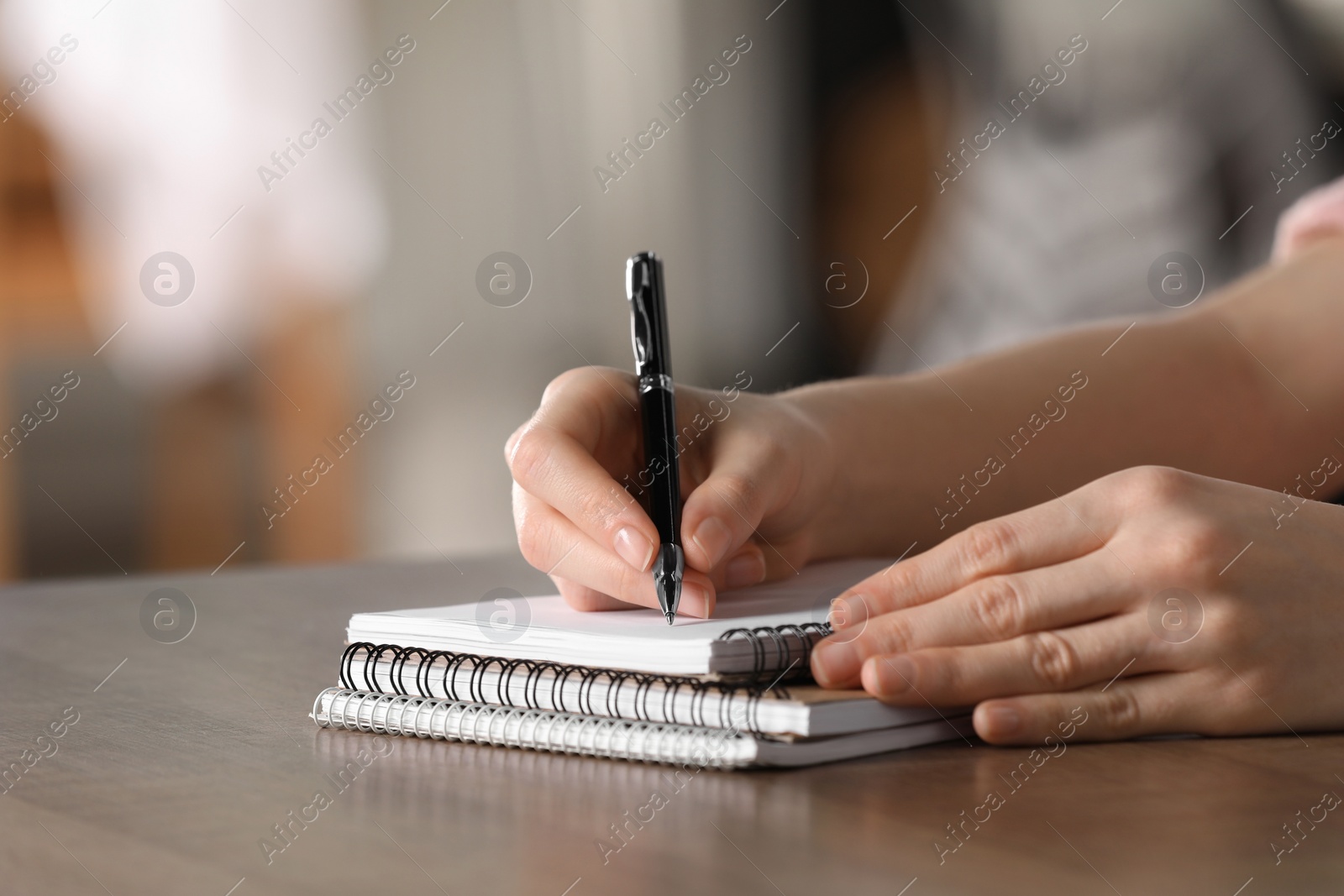 Photo of Woman writing in notebook at wooden table, closeup