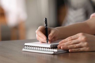 Woman writing in notebook at wooden table, closeup