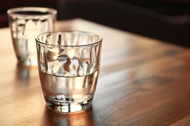 Glasses of water on wooden table in cafe. Space for text