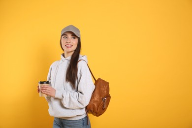 Photo of Beautiful young woman with stylish leather backpack and cup of coffee on yellow background. Space for text