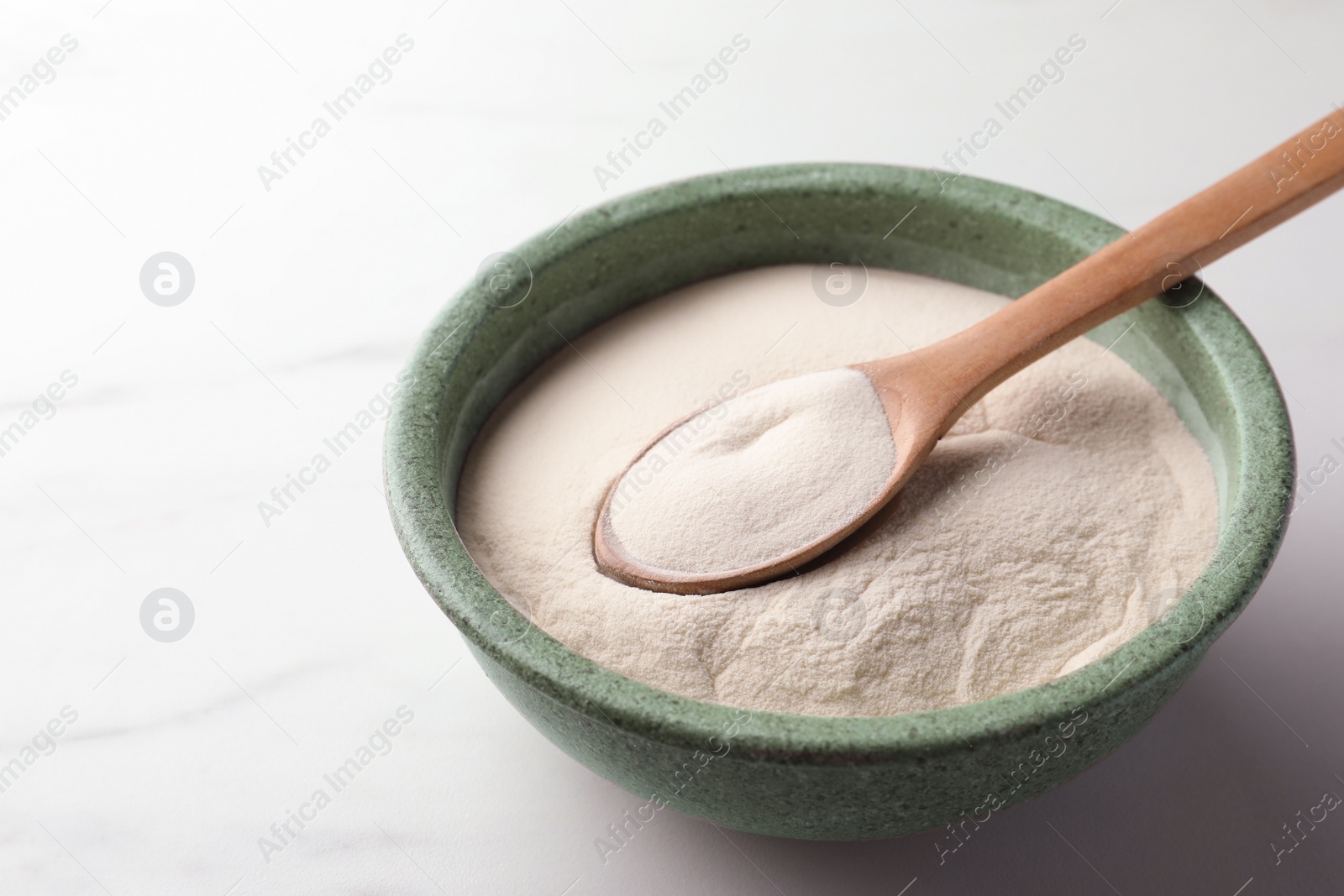 Photo of Bowl and spoon of agar-agar powder on white marble table, closeup