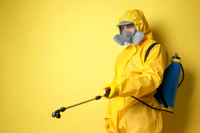Photo of Man wearing protective suit with insecticide sprayer on yellow background, space for text. Pest control