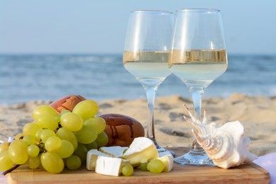 Photo of Glasses with white wine and snacks for beach picnic on sandy seashore, closeup