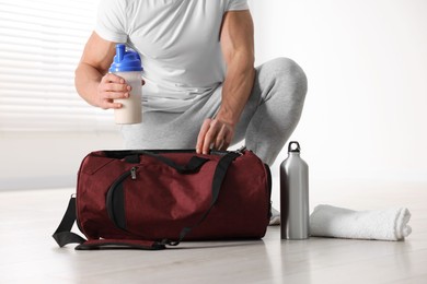 Photo of Young man putting shaker with protein into bag indoors, closeup