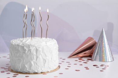 Photo of Delicious cake with burning candles and party hats on white table. Space for text