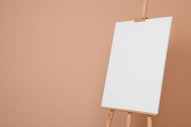 Photo of Wooden easel with blank canvas on beige background. Space for text