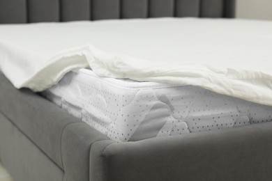 Photo of New soft mattress with bedsheet on bed, closeup