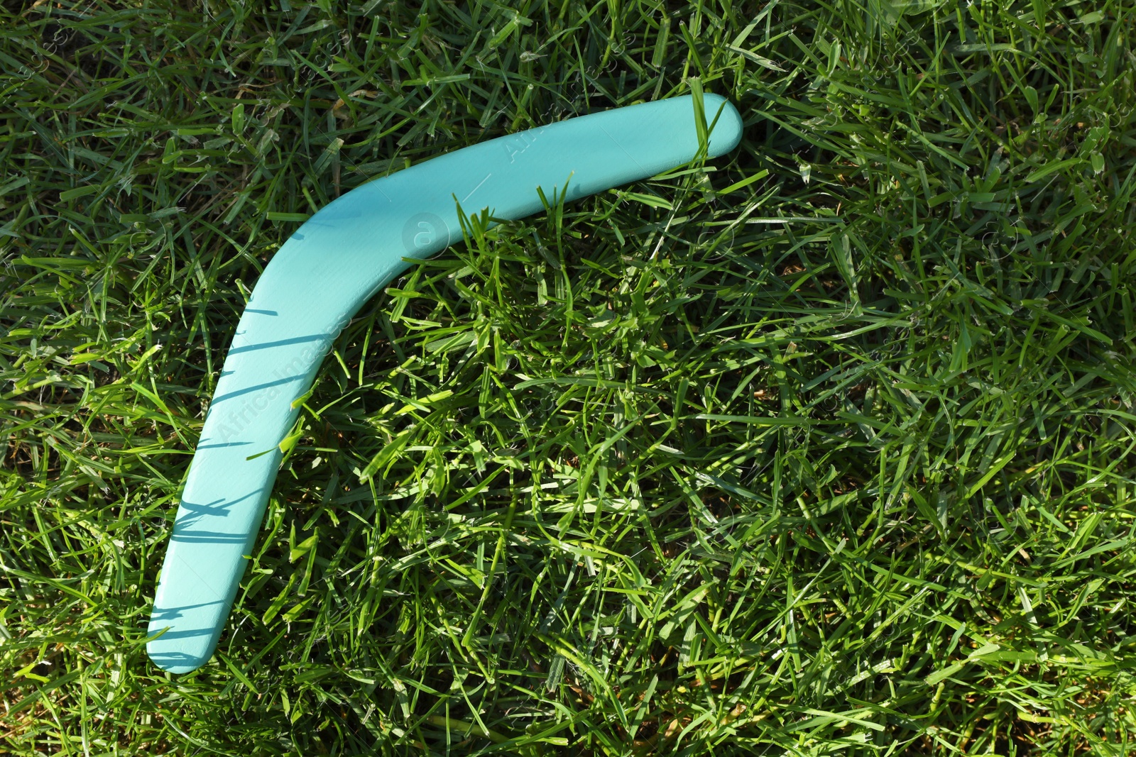 Photo of Turquoise wooden boomerang on green grass outdoors, above view. Space for text