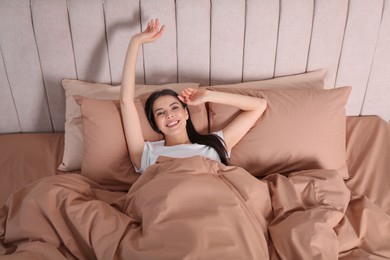Photo of Woman awakening in comfortable bed with beige linens, above view