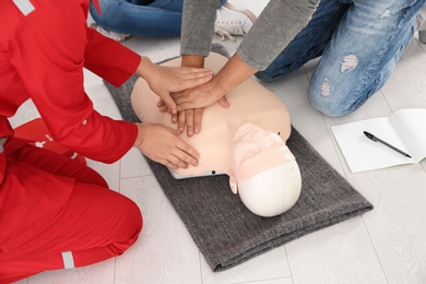 Photo of Group of people with instructor practicing CPR on mannequin at first aid class indoors, closeup
