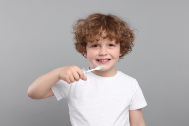 Photo of Cute little boy holding plastic toothbrush on light grey background