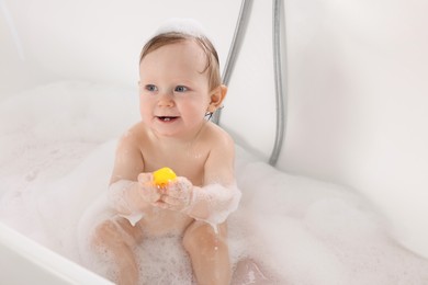 Photo of Cute little baby with toy taking foamy bath at home