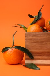 Photo of Wooden crate with fresh ripe tangerines and leaves on orange table