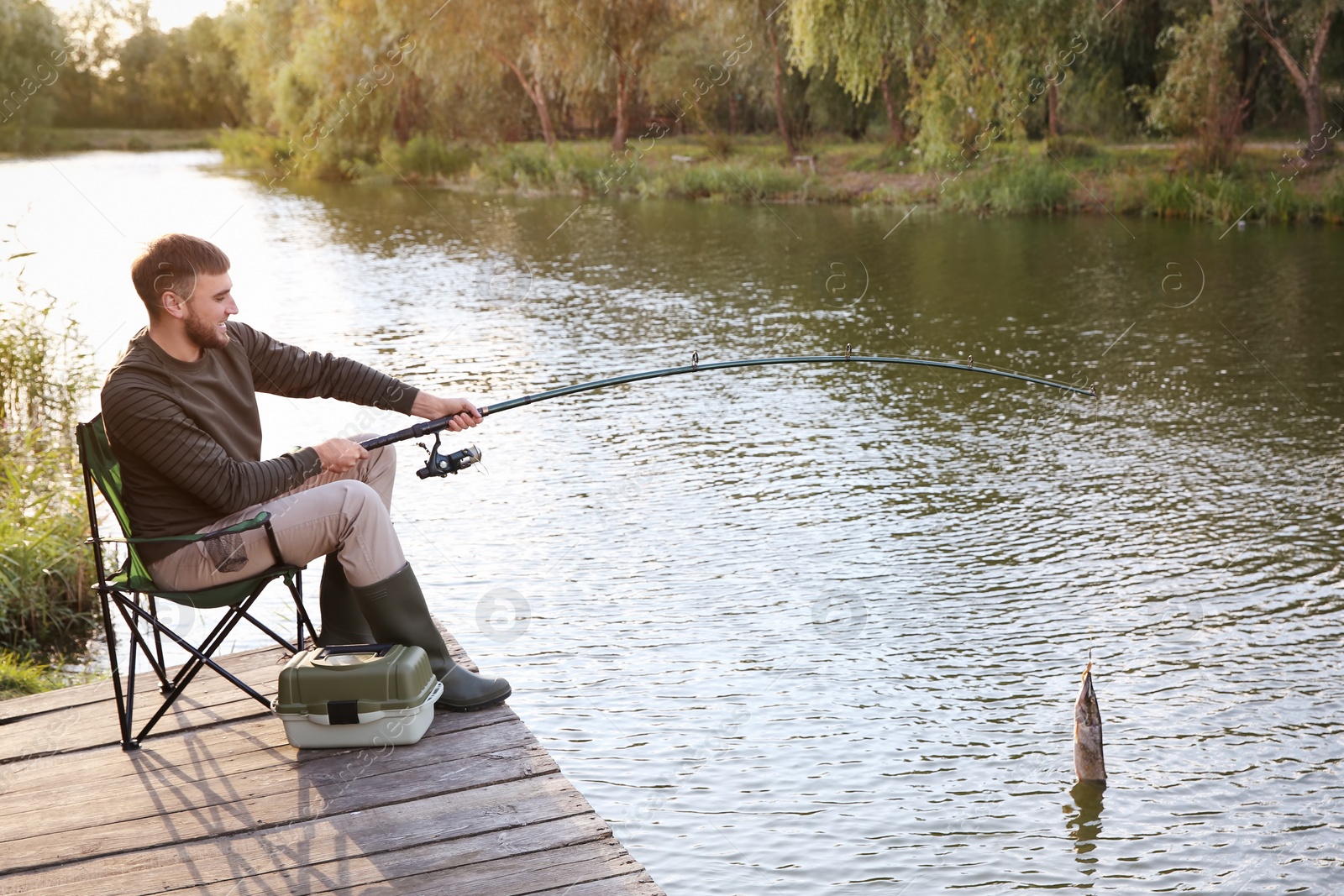 Photo of Man with rod fishing on wooden pier at riverside. Recreational activity