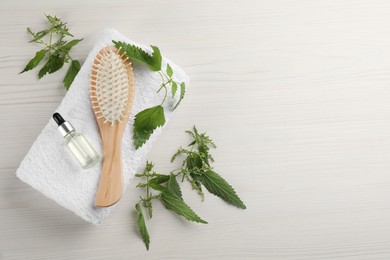 Photo of Stinging nettle, extract, towel and brush on white wooden background, flat lay with space for text. Natural hair care
