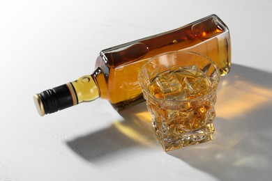 Photo of Whiskey with ice cubes in glass and bottle on white table