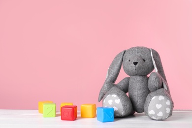 Photo of Adorable toy bunny and plastic cubes on table against color background, space for text. Child room elements