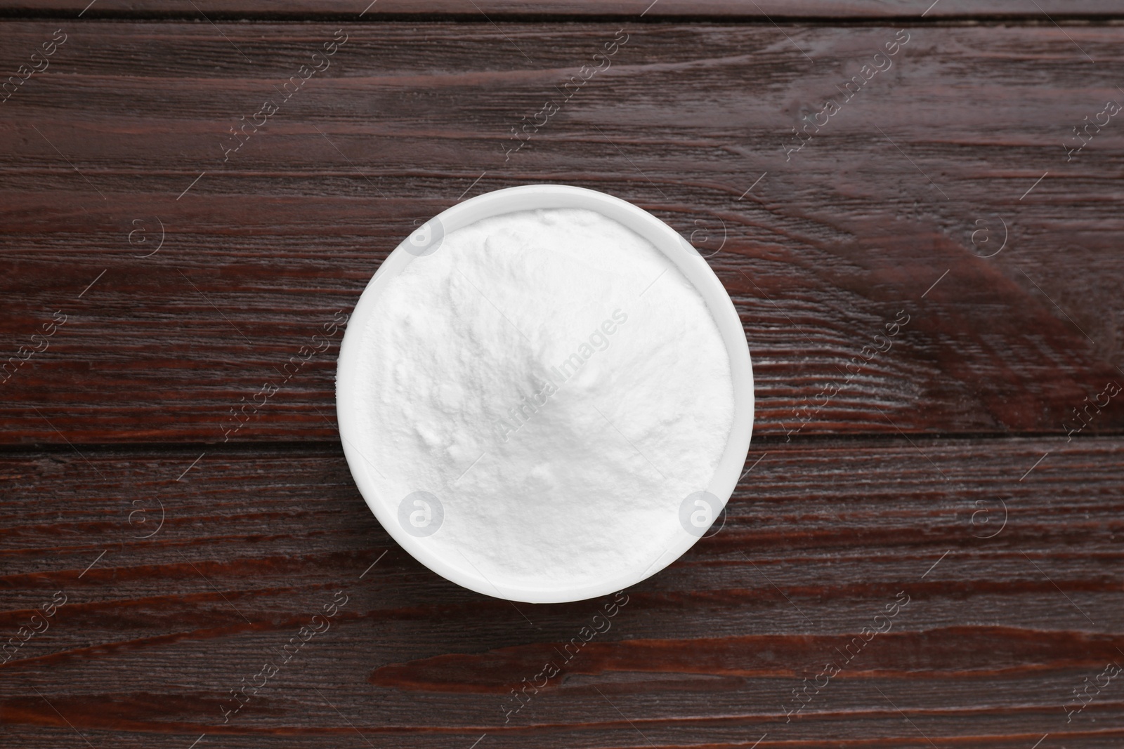 Photo of Bowl of sweet powdered fructose on black wooden table, top view