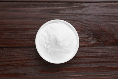 Bowl of sweet powdered fructose on black wooden table, top view