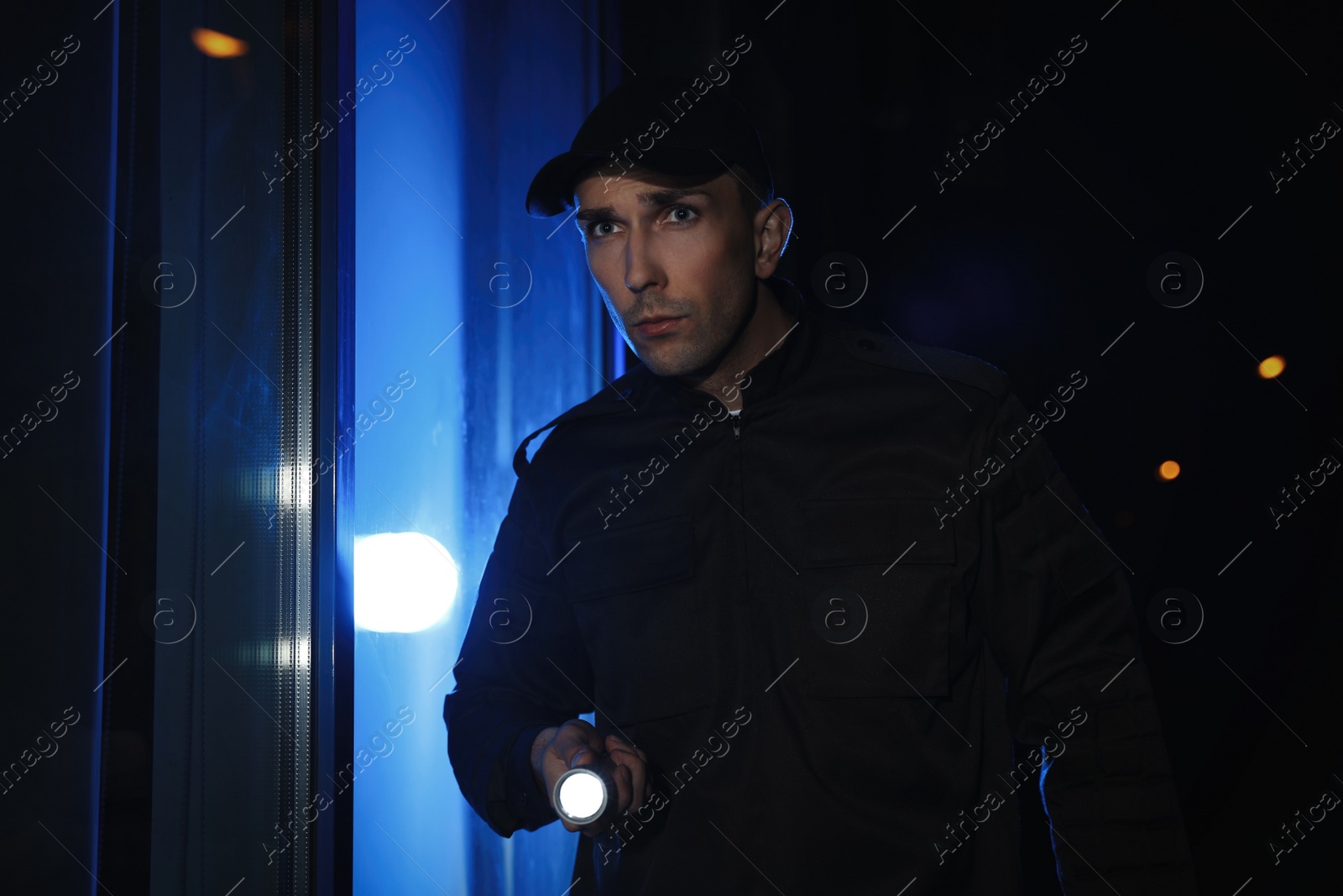 Photo of Male security guard with flashlight in dark corridor