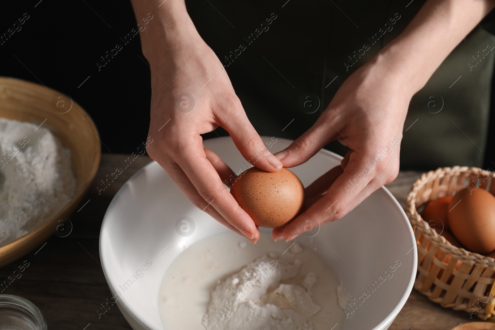 Photo of Making bread. Woman adding egg into dough at wooden table on dark background, closeup