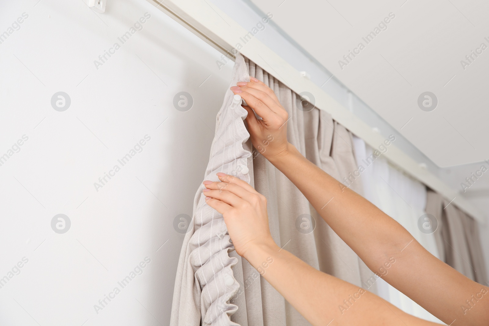 Photo of Woman hanging window curtain indoors, closeup. Interior decor element